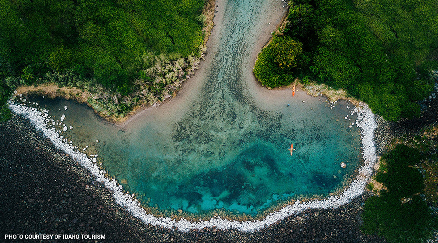 Aerial view of Blue Heart Springs in Southern Idaho with crystal-clear turquoise water, lush shoreline, and kayakers exploring the spring.
