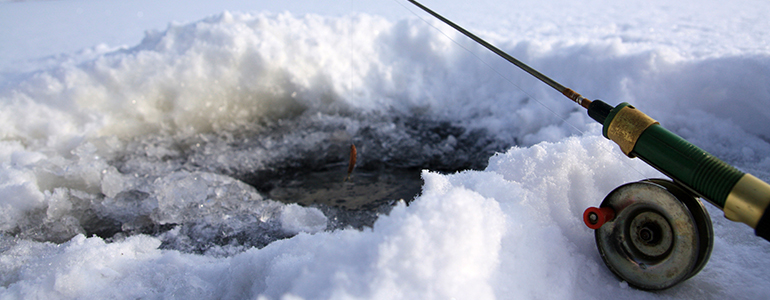 A closeup of a fishing pole laying on ice next to an ice fishing hole.