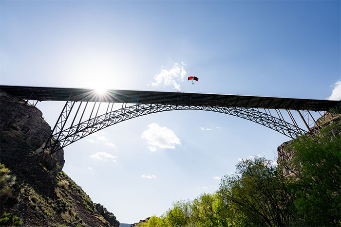 A BASE jumper with a red and grey parachute gliding down from the Perrine Bridge.