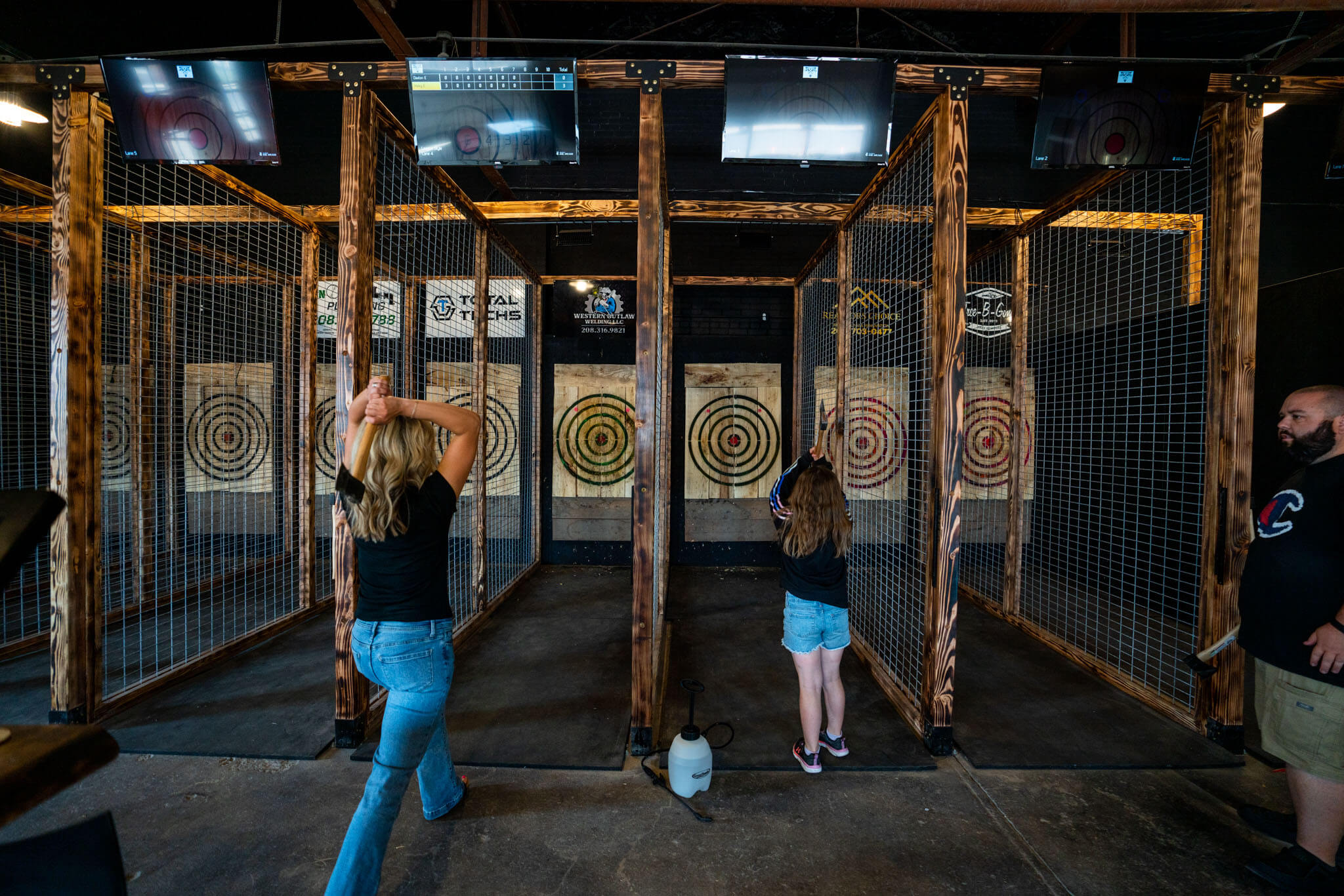 A woman and child prepare to throw axes at wooden targets in an indoor facility as a man watches on.