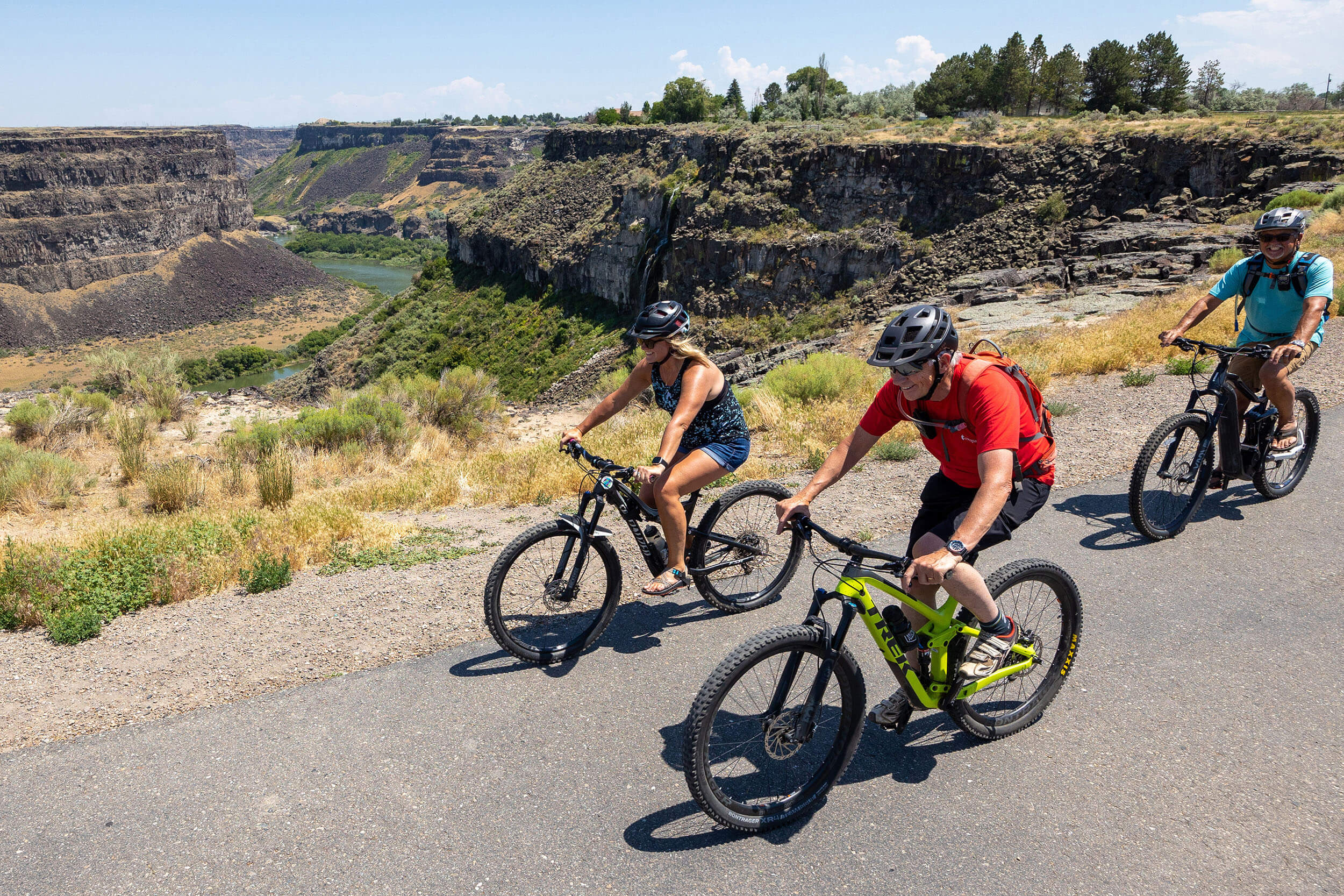 Three bikers with helmets on ride together on a road above the Snake River Canyon.