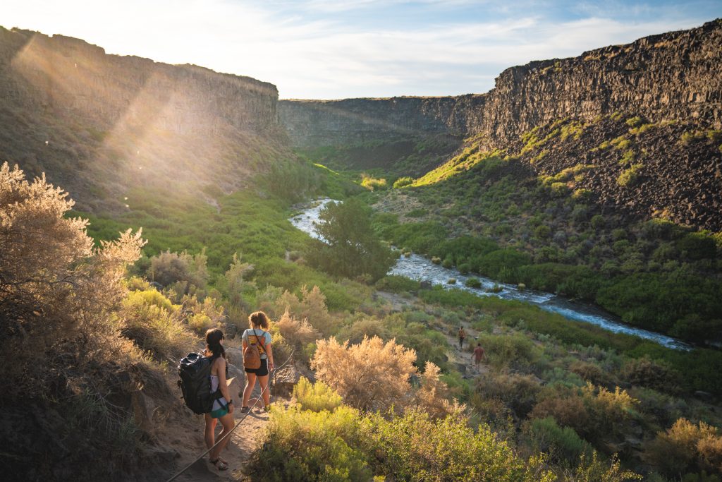 Two people in summer hiking gear descend on a trail into Box Canyon Nature Preserve.