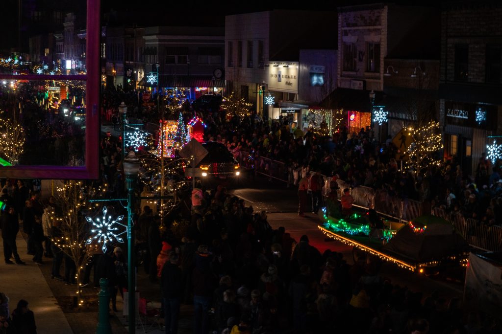 An overhead shot of crowds watching a Christmas parade in a festively lit downtown.