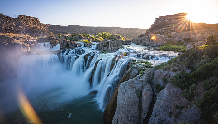 A side view of Shoshone Falls surrounded by large rock formations and greenery.