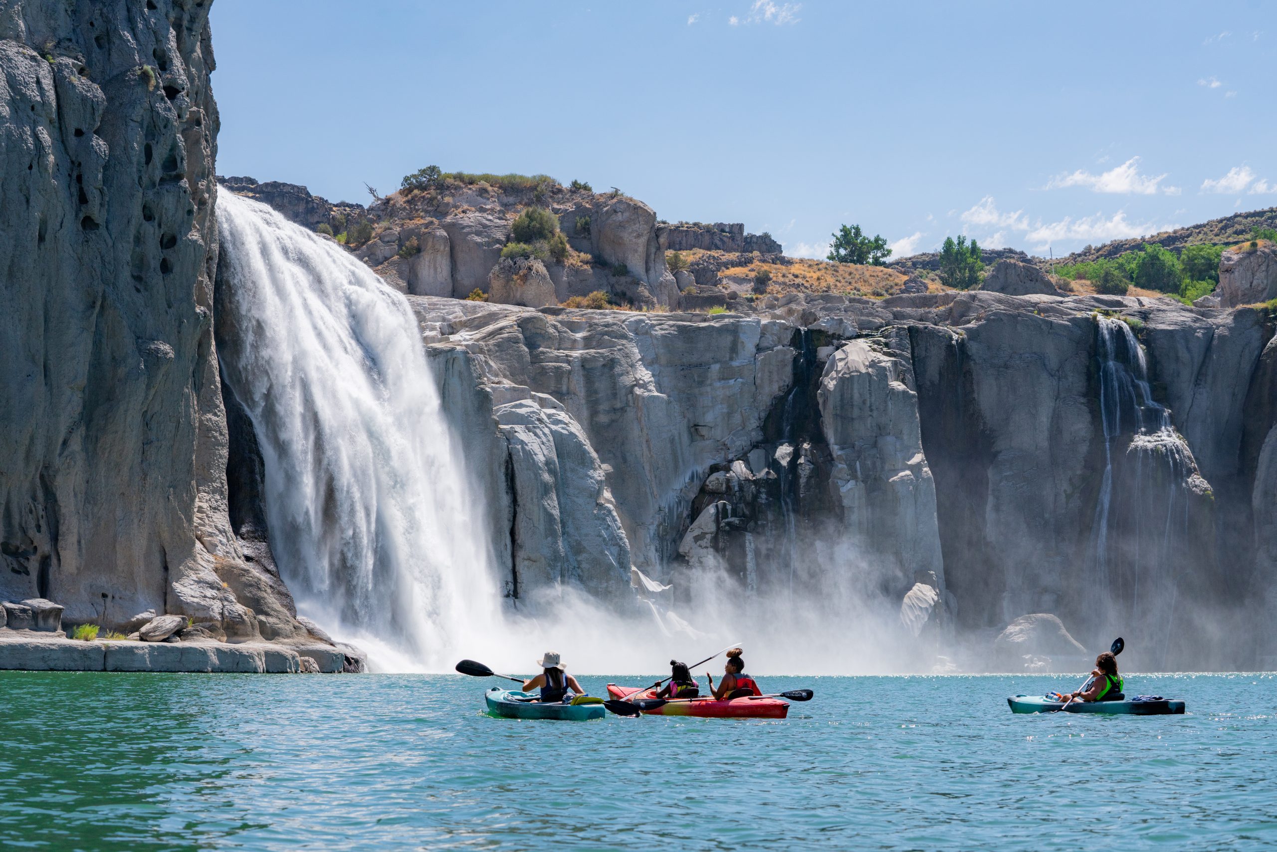 A group of people kayaking in front Shoshone Falls, and in the background, large rock walls with water trickling down them.
