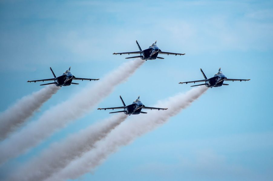 Four blue aircraft streak gray smoke trails across a wide, open sky.