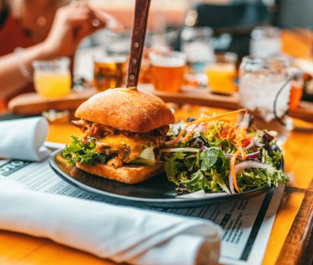Cheesy sandwich with a knife, salad on a plate, surrounded by colorful drinks on a table.