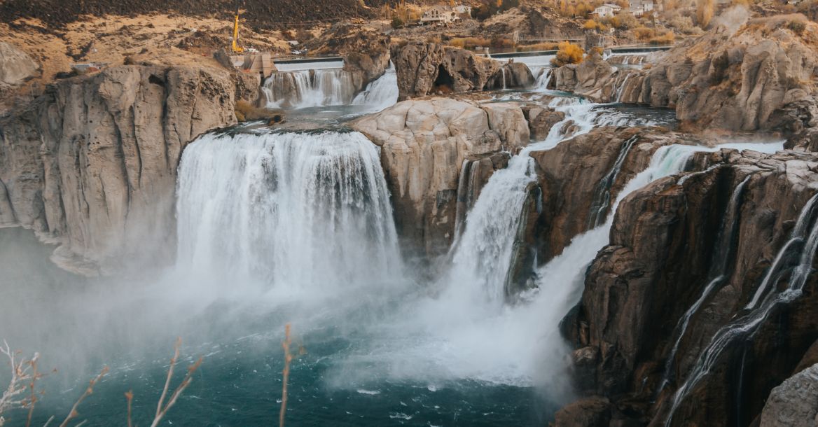 A waterfall cascading from the side of a cliff surrounded by brush and rocky landscapes.