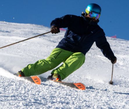 A skier leans forward, kicking up snow with poles while sliding down a slope at Pomerelle Resort, wearing a helmet and goggles under a blue sky.