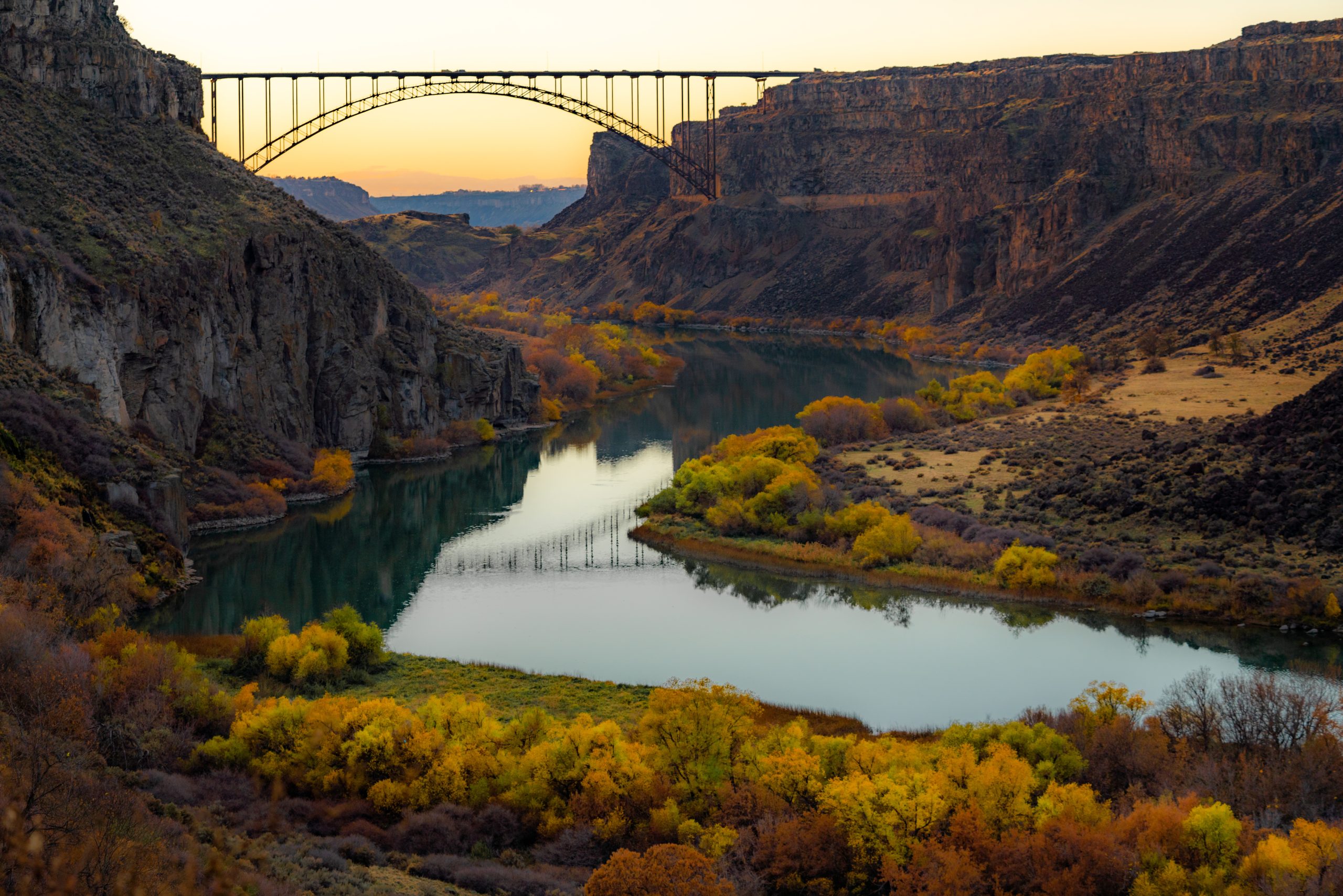 The Perrine Bridge at sunset, spanning the Snake River Canyon in Twin Falls, Idaho surrounded by vibrant fall foliage.